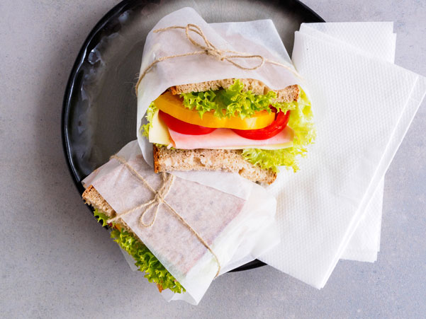 Belegte Brote mit Schinken, Käse, Paprika und Salat in Umverpackung aus Papier und Naturkordel