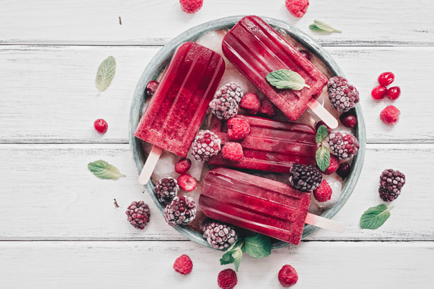 Rotes Himbeereis am Stil auf Teller liegend, dekoriert mit frostigen Himbeeren