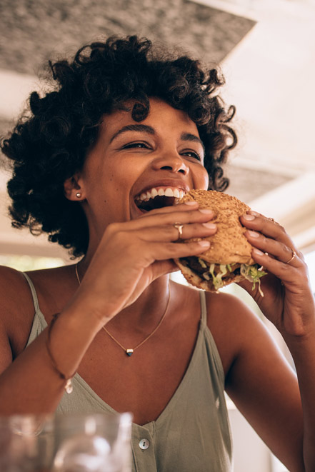 Frau die lachend in einen Hamburger beißt
