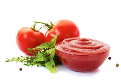 Neben einer Schale mit Ketchup liegen zwei Tomaten und Kräuter